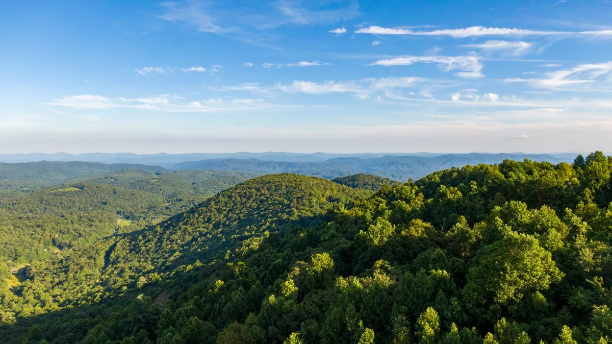 A sweeping view of rolling hills, dense greenery, and distant mountains under an expansive sky. The scene highlights the tranquil and scenic beauty surrounding the cabin, offering a glimpse of the landscapes accessible from the Blue Ridge Parkway and nearby nature trails.