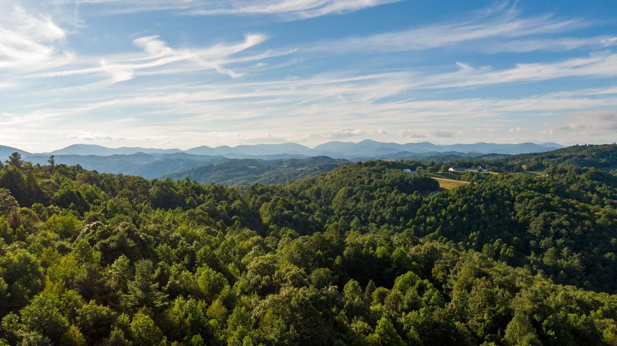 An expansive vista of rolling mountains and dense forest, with a clear sky overhead. The scene captures the peacefulness and grandeur of the high country, evoking the sense of adventure and discovery that awaits families staying at the cabin.