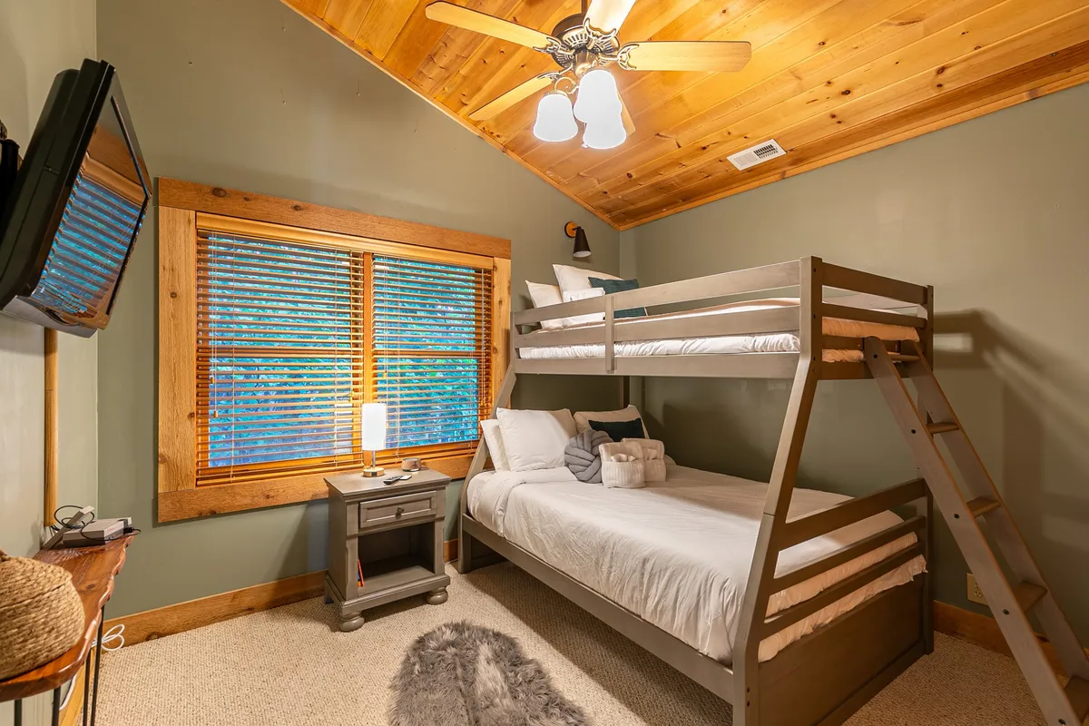 A cheerful bedroom featuring a twin-over-full bunk bed beside a window, with a nightstand and lamp creating a playful yet restful environment. The layout is ideal for children or friends sharing the space.