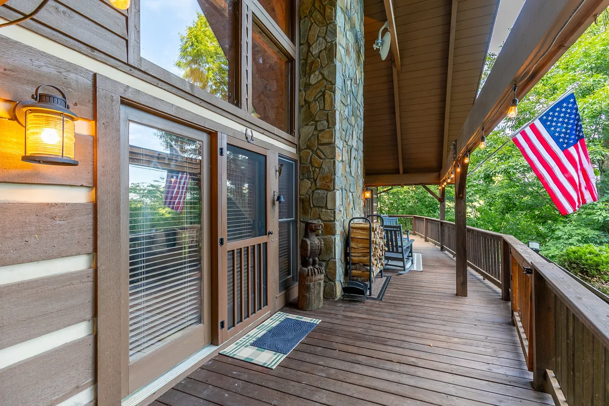 This exterior image features the cabin's inviting wooden deck, complete with outdoor seating and an American flag. The stone wall and lush surroundings evoke a welcoming, family-friendly atmosphere and provide an immediate connection to the natural landscape, perfect for relaxing after outdoor adventures.